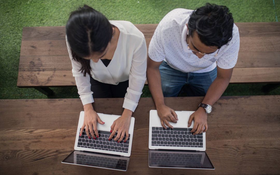 Couple using laptops at picnic table